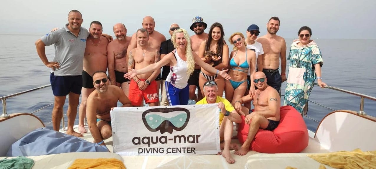 Grup de scafandri pe un vas, cu bannerul Aqua-Mar Diving Center