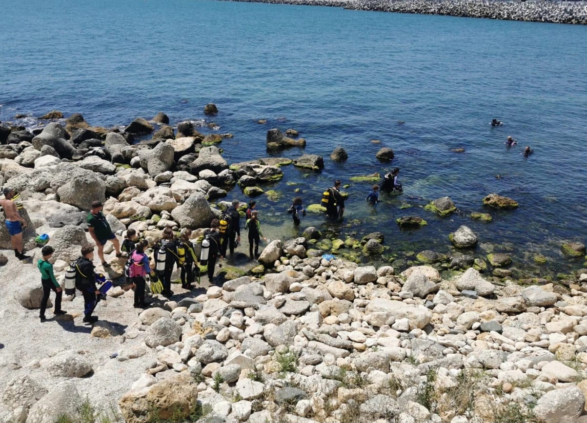 Grup de scafandri care intră în mare de pe un țărm stâncos